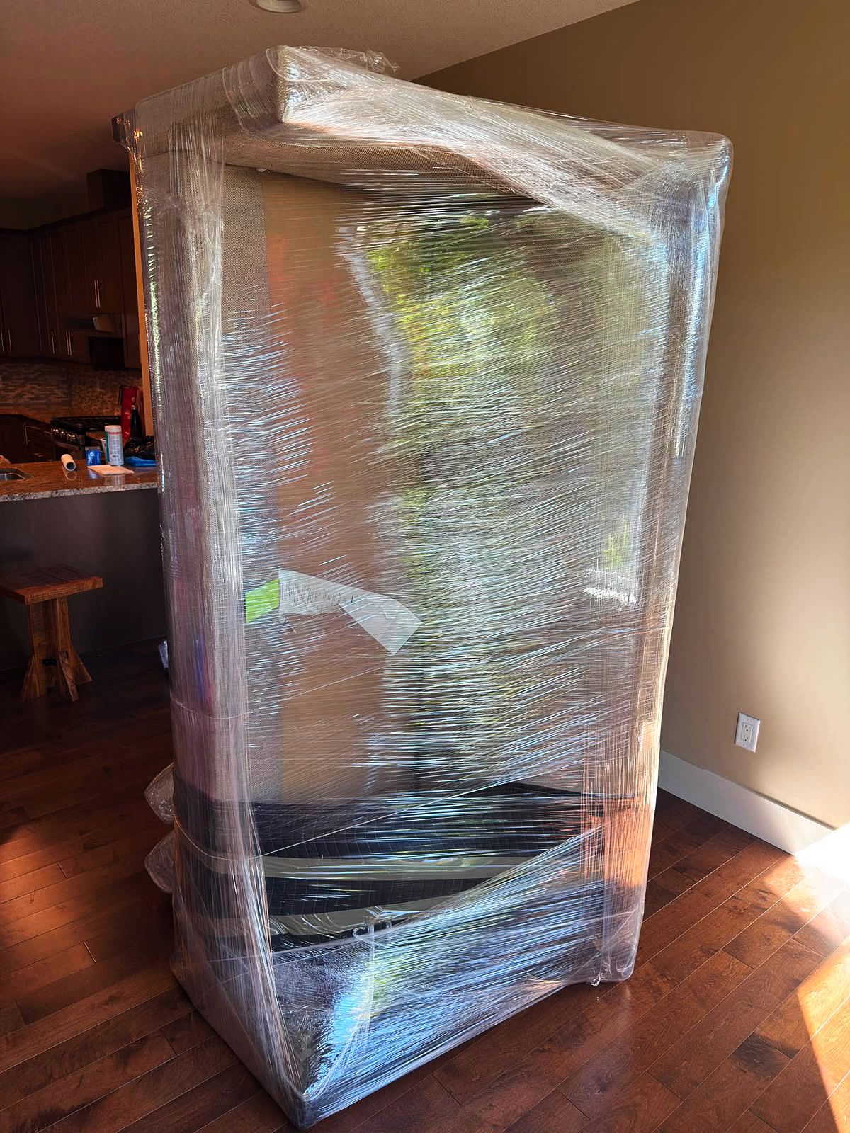 Large wardrobe wrapped in stretch film beside a bright kitchen